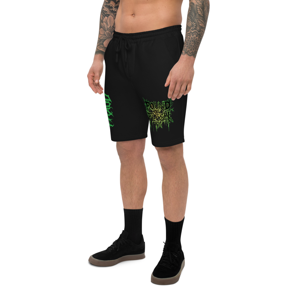 Man wearing black shorts with th ePound of Flesh TX logo outlined in green and yellow on the left leg, and the word Fraud in a gothic fint on the right leg